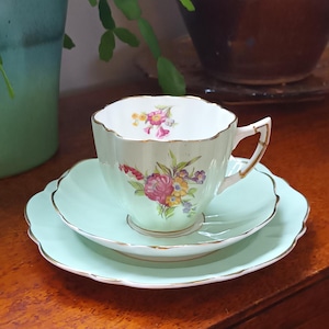Peut inclure: Un ensemble de tasse et soucoupe à thé vintage avec un motif floral délicat dans des tons de rose, jaune et vert. L'ensemble est en porcelaine fine et a un glaçage vert clair.