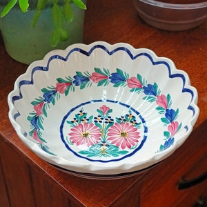 Puede incluir: Un tazón de cerámica blanca con un borde festoneado y un diseño floral azul y rosa. El tazón tiene un fondo blanco con un borde floral azul y rosa y un motivo floral central.