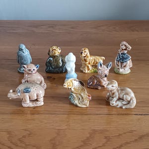 May include: A collection of small ceramic animal figurines, including a penguin, dog, fish, deer, and rabbit. The figurines are in various colors and poses, set on a wooden surface.