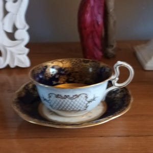 May include: A blue and gold teacup and saucer set with intricate floral designs. The cup has a white interior and a gold rim. The saucer has a blue and gold rim.