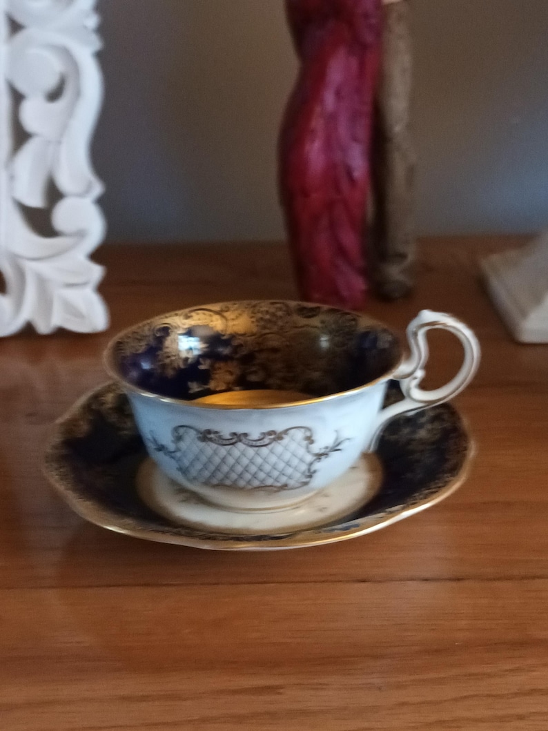 May include: A blue and gold teacup and saucer set with intricate floral designs. The cup has a white interior and a gold rim. The saucer has a blue and gold rim.