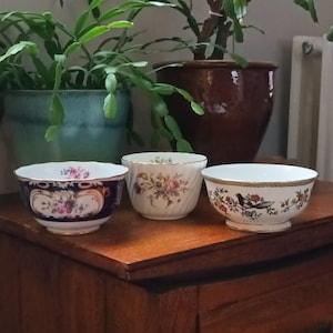 May include: Three vintage porcelain bowls with floral and bird designs. The bowls are on a wooden surface.