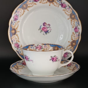 May include: A white teacup and saucer set with a floral design. The cup and saucer have a blue and gold trim. The saucer has a scalloped edge.