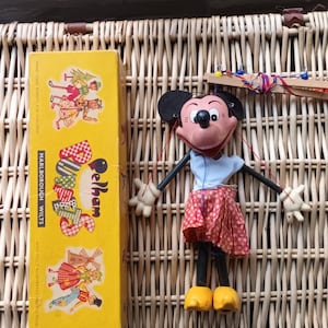 Puede incluir: Una marioneta Pelham vintage de un personaje de ratón, con una camisa azul y una falda roja de lunares, con zapatos amarillos. La marioneta es en blanco y negro con nariz y boca rojas. Junto a una caja amarilla con el texto "Pelham Marlborough Wilts".