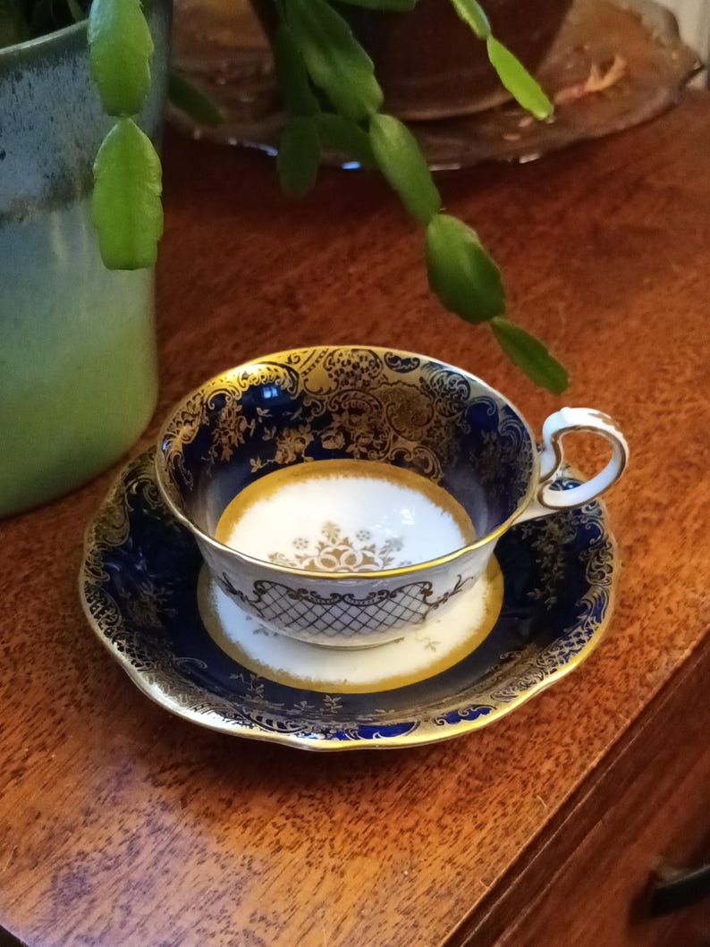 May include: A blue and gold teacup and saucer set with intricate floral and geometric patterns. The cup has a white interior and a gold rim.