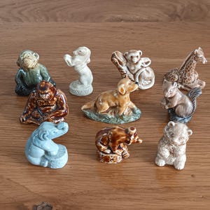 以下が含まれることがあります： 猿、象、熊、犬、リス、キリンなど、セラミック製の動物フィギュアのコレクション。 フィギュアは様々な色で塗装されており、木製の表面に置かれています。