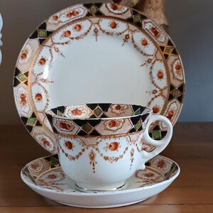 May include: A vintage teacup and saucer set with a black, green, gold, and red geometric pattern. The set features a white background with a delicate floral design.