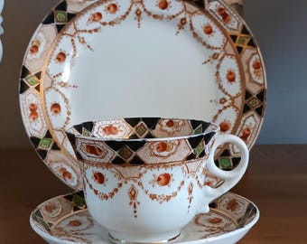 May include: A vintage teacup and saucer set with a black, green, gold, and red geometric pattern. The set features a white background with a delicate floral design.