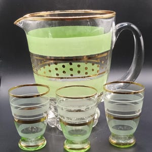 Könnte beinhalten: Ein Set aus vier Vintage-Getränkegläsern aus Glas mit grünem und goldenem Design. Das Set enthält eine Karaffe und drei kleine Gläser. Die Karaffe hat ein grünes Band und goldene Punkte. Die Gläser haben ein grünes Band und goldene Streifen.