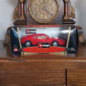 Könnte beinhalten: Ein rotes Ferrari 348 Modellauto in der Originalverpackung. Das Modell ist ein Nachbau im Maßstab 1:24 mit detaillierten Merkmalen. Die Box hat das "burago" Logo und die Worte "Ferrari 348 tb 1993".