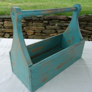 May include: A teal blue wooden carrying box with a handle. The box has a distressed finish and is perfect for carrying small items.