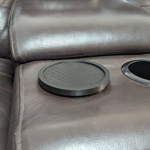 May include: A close-up of a brown leather sofa with two cup holders. One cup holder has a black rubber coaster inside.