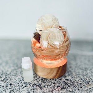 May include: A glass diffuser with a wooden base and a small bottle of essential oil. The diffuser is filled with dried flowers and cinnamon sticks. The base of the diffuser is lit up with a warm orange glow.