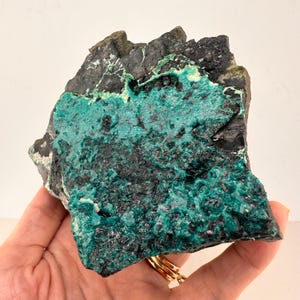 May include: A piece of raw rock displaying a vivid colour contrast. The base is a dark, nearly black stone, covered with bright turquoise and teal mineral deposits. The texture is rough and irregular, revealing natural geological patterns.