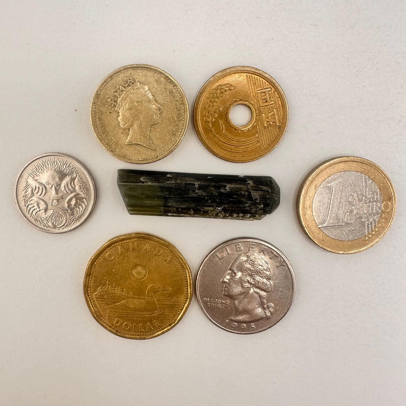 May include: An assortment of coins from different countries, including a Canadian dollar, a US quarter, a British coin, a Japanese coin, and a Euro coin. A dark green, elongated gemstone is also present.