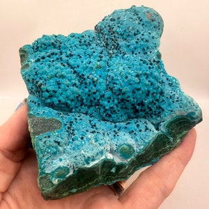 May include: A large, irregularly shaped piece of blue and green chrysocolla with black inclusions. The chrysocolla has a smooth, polished surface and a botryoidal texture.