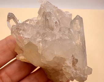 May include: A cluster of clear quartz crystals with a rough, natural texture. The crystals are arranged in a cluster, with some pointing upwards and others pointing downwards. The crystals are translucent and have a slight yellow tint.