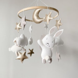 May include: A white felt bunny with a gold crescent moon and stars hanging from a wooden ring. The mobile is made of felt and is perfect for a baby's nursery.