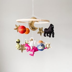 May include: A baby mobile with a wooden ring, felt planets, stars, a felt astronaut, a felt dinosaur, a felt alien, and a felt gorilla.