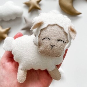 May include: A white felt sheep with a beige face and closed eyes. The sheep has a fluffy white body and small beige ears.