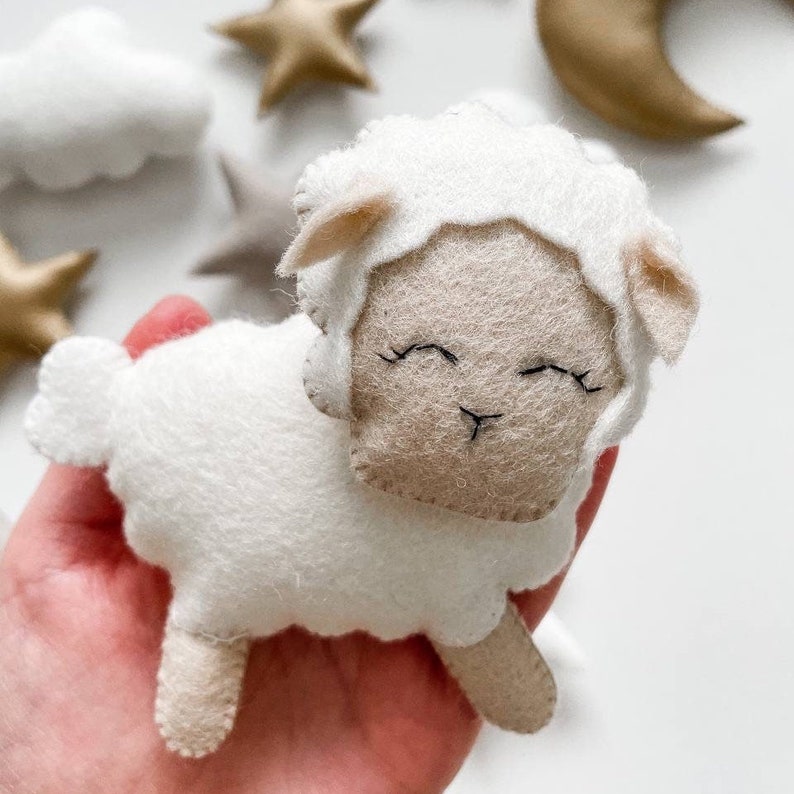 May include: A white felt sheep with a beige face and closed eyes. The sheep has a fluffy white body and small beige ears.