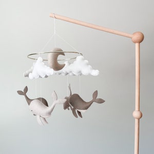 May include: A wooden mobile stand with a white and beige felt mobile hanging from it. The mobile features two whales, clouds, and a crescent moon.