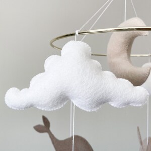 May include: A white felt cloud mobile hanging from a gold metal ring. The cloud is fluffy and has a slightly irregular shape.