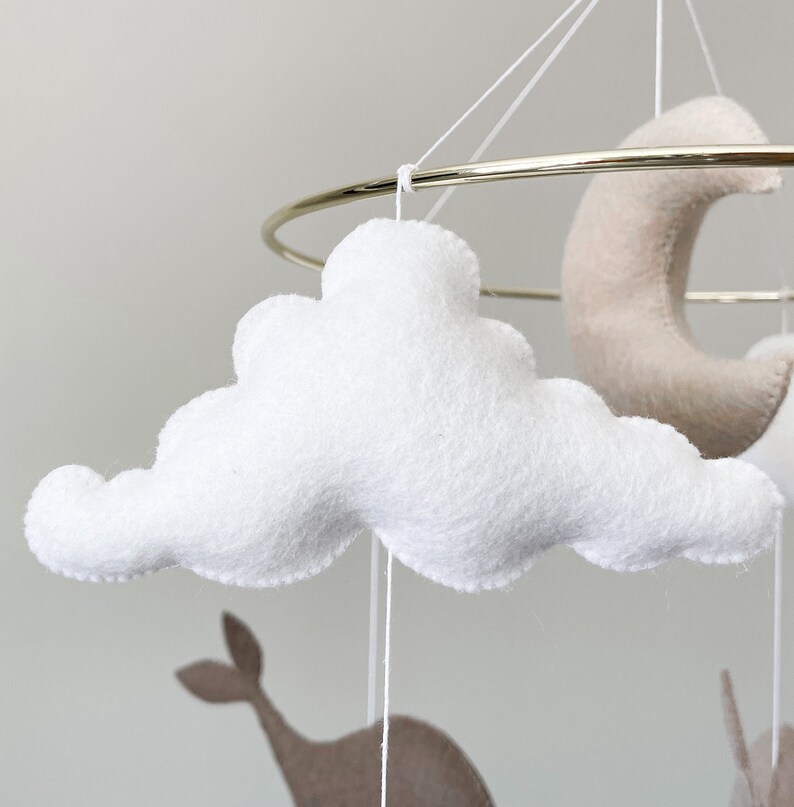 May include: A white felt cloud mobile hanging from a gold metal ring. The cloud is fluffy and has a slightly irregular shape.