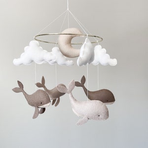 May include: A baby mobile with a crescent moon, clouds, and whales made of felt. The mobile is suspended from a gold ring.