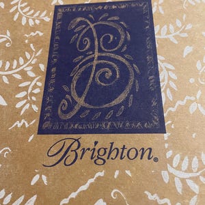 Peut inclure: Un sac en papier brun avec un motif floral blanc. Le sac a un carr&eacute; bleu avec une lettre "B" stylis&eacute;e dor&eacute;e &agrave; l'int&eacute;rieur. Le texte "Brighton." est imprim&eacute; en bleu sous le carr&eacute;.