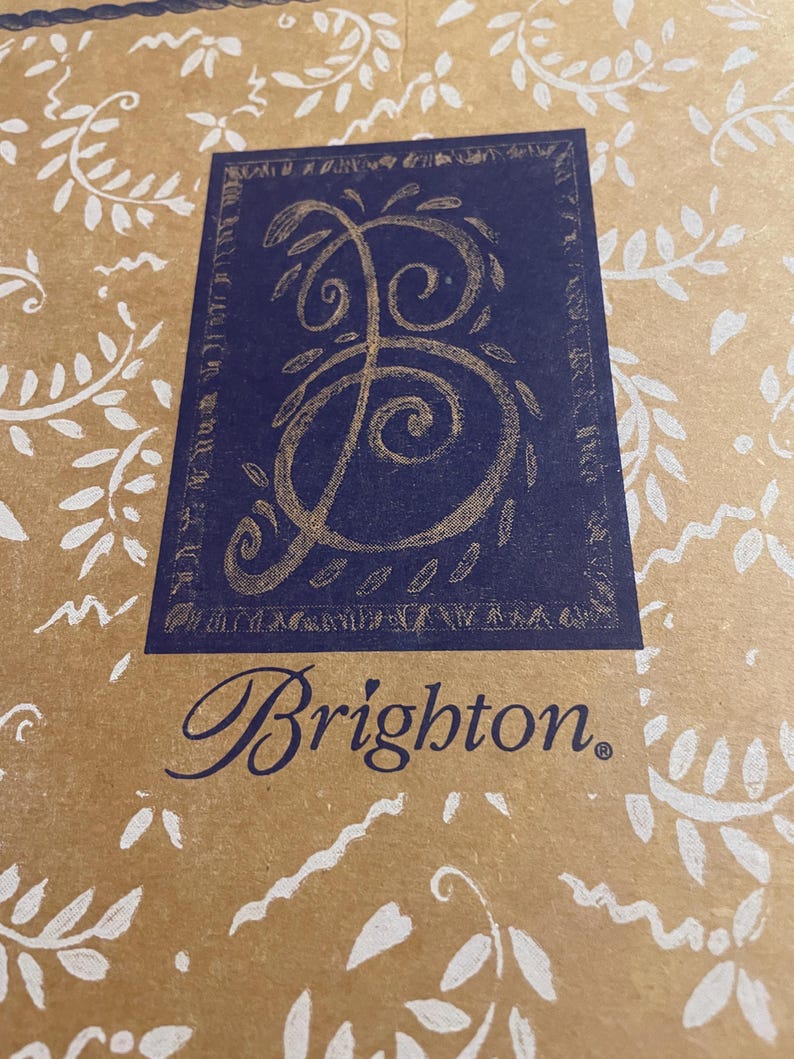 Peut inclure: Un sac en papier brun avec un motif floral blanc. Le sac a un carr&eacute; bleu avec une lettre "B" stylis&eacute;e dor&eacute;e &agrave; l'int&eacute;rieur. Le texte "Brighton." est imprim&eacute; en bleu sous le carr&eacute;.