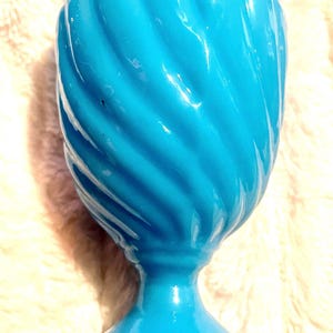 May include: A turquoise blue ceramic vase with a swirl design. The vase has a wide base and a narrow opening.