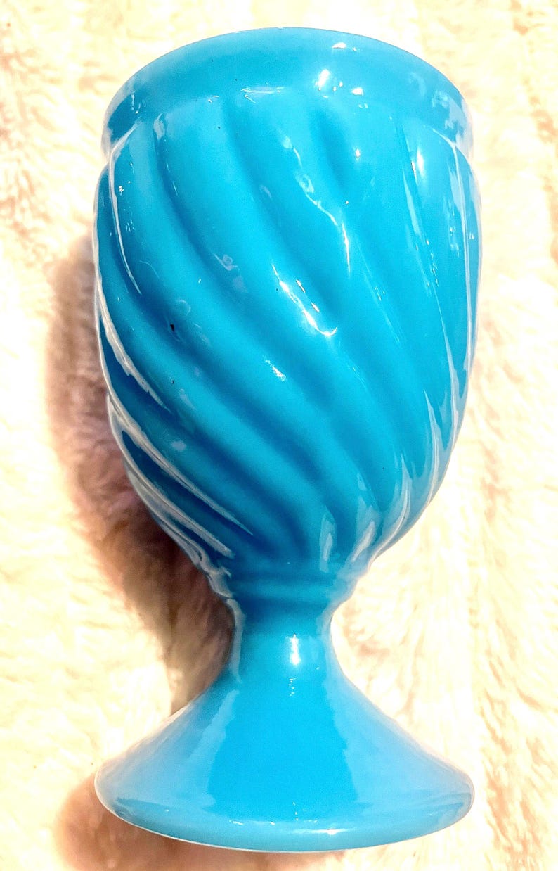 May include: A turquoise blue ceramic vase with a swirl design. The vase has a wide base and a narrow opening.