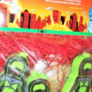 May include: A string light set with the text "MARS ATTACKS!". The packaging features a city under attack by UFOs. The set includes 10 mischievous MARS ATTACKS! covers. The string is 14 feet long.