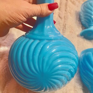 May include: A set of blue glass decanter and glasses with a swirl design. The decanter has a tall, slender neck and a round body. The glasses are shorter and have a wider bowl.