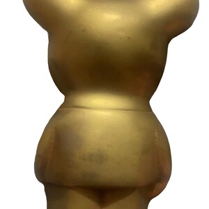 May include: A gold-colored ceramic bear figurine. The bear is standing upright with its arms at its sides. The bear has a simple, rounded design.