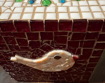 May include: A mosaic tissue box featuring a bird design. The box is primarily red with white and red tiles. The top has a circular opening surrounded by green, blue, and clear glass beads. A mosaic bird is on the front.
