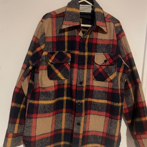 May include: A long-sleeved flannel shirt with a plaid pattern in shades of red, black, yellow, and brown. The shirt has a button-up front and two chest pockets. The label on the shirt reads "Oshman's".