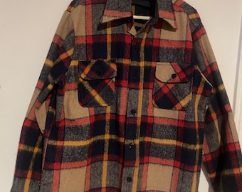 May include: A long-sleeved flannel shirt with a plaid pattern in shades of red, black, yellow, and brown. The shirt has a button-up front and two chest pockets. The label on the shirt reads "Oshman's".