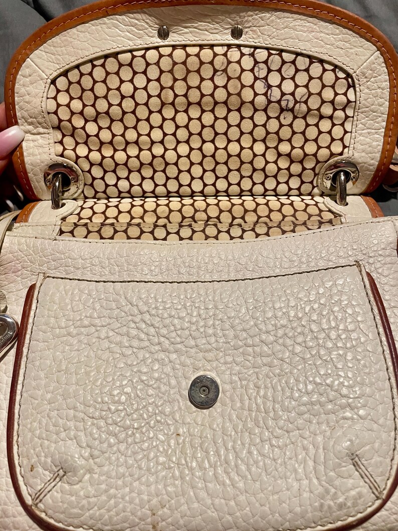 Peut inclure: Sac &agrave; main en cuir blanc avec une doublure &agrave; pois marrons. Le sac a une fermeture &agrave; rabat et une petite poche sur le devant.
