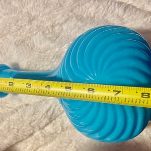 May include: A turquoise blue glass vase with a swirl design and a long neck. The vase is 8 inches tall.