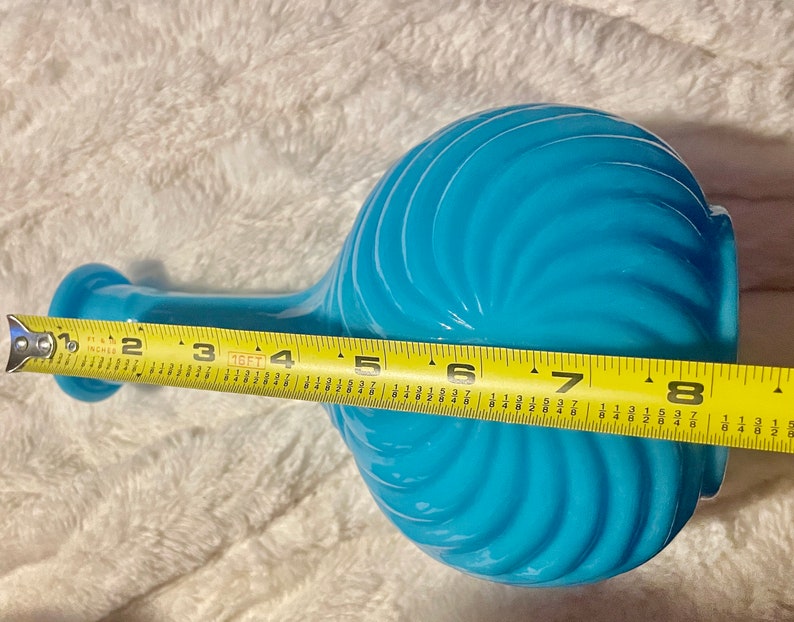 May include: A turquoise blue glass vase with a swirl design and a long neck. The vase is 8 inches tall.