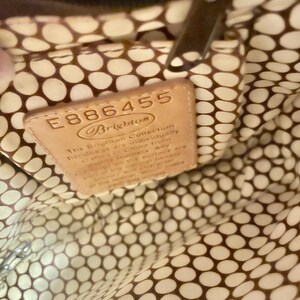Peut inclure: Gros plan de l'int&eacute;rieur d'un sac &agrave; main brun avec une doublure &agrave; pois blancs et bruns. Une &eacute;tiquette en cuir brun avec le texte "E886455 Brighton The Brighton Collection handbags are individually crafted in China from quality leathers. Any m&eacute;lange on the surface are..." est visible.