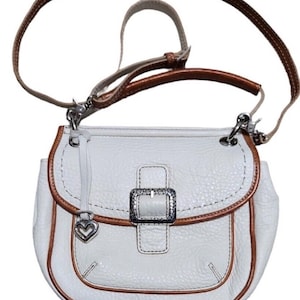 Peut inclure: Sac &agrave; bandouli&egrave;re en cuir blanc avec une bordure en cuir marron et une boucle argent&eacute;e. Le sac est dot&eacute; d'un charm en forme de c&oelig;ur.