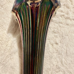May include: A tall, fluted glass vase featuring a vibrant, iridescent finish with shifting hues of deep green, purple, and gold. The surface is characterized by vertical ridges that extend from the base to the scalloped, flared rim.