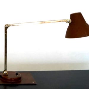 May include: A brown desk lamp with a brass-colored adjustable arm and a conical shade. The lamp has a wooden base and a power cord. The lamp is designed for desk use and provides focused lighting.