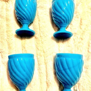 May include: Four blue egg cups with a swirl design. The cups are made of ceramic and have a glossy finish.