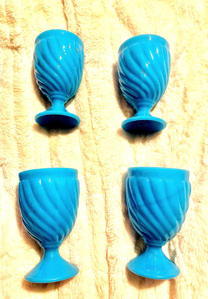 May include: Four blue egg cups with a swirl design. The cups are made of ceramic and have a glossy finish.
