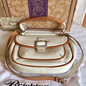 Peut inclure: Un sac &agrave; main Brighton en cuir blanc avec une garniture en cuir marron et une boucle argent&eacute;e. Le sac a une poign&eacute;e sup&eacute;rieure et une bandouli&egrave;re.