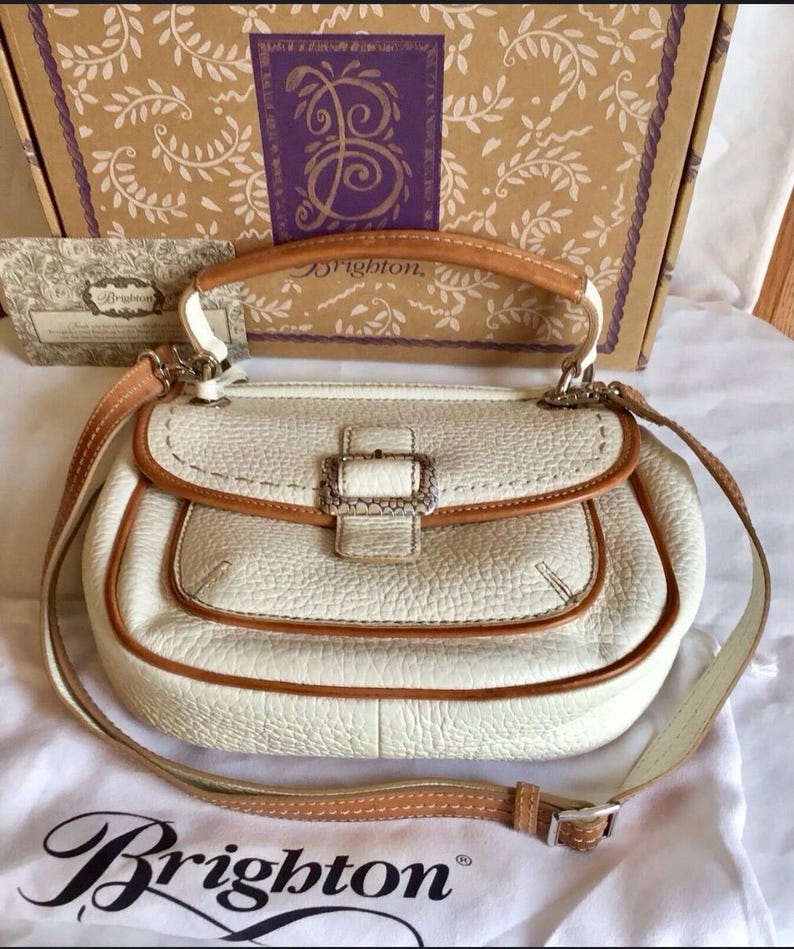 Peut inclure: Un sac &agrave; main Brighton en cuir blanc avec une garniture en cuir marron et une boucle argent&eacute;e. Le sac a une poign&eacute;e sup&eacute;rieure et une bandouli&egrave;re.